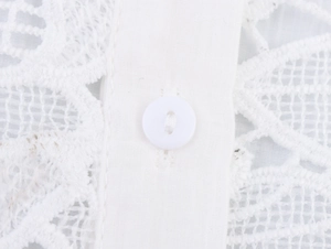 Detailed macro view of white lace fabric pattern and button placket on a women blouse