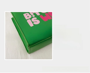 Detail showing high-quality green leather stitching and pink typographic print on handbag