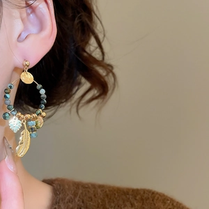 Detail of bohemian gold feather earrings with turquoise beads worn by a model