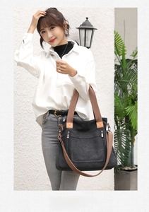 Minimalist black canvas tote bag with brown handles shown in a lifestyle street shot