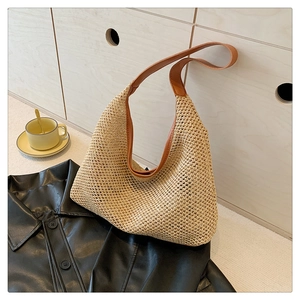 Detail of woven straw tote bag with brown leather handles placed near wooden cabinet