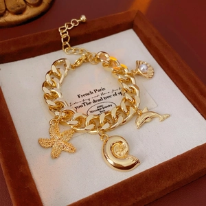 Gold chunky chain bracelet with starfish dolphin and pearl shell charms on velvet display