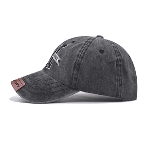 Détail de la casquette en jean gris délavé avec broderie E blanche et écusson en cuir brun