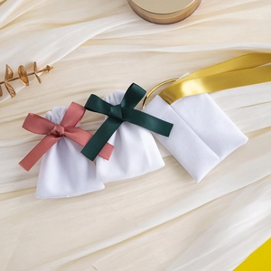 Three white velvet jewelry pouches with pink, green and gold satin ribbon bows