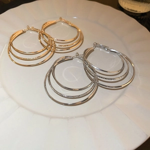 Orecchini a cerchio multistrato in metallo dorato e argento su vassoio in ceramica bianca