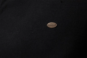 Macro shot of knitted fabric texture and a bronze metal logo badge on a black cardigan