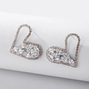 Detail view of heart shaped silver earrings with rhinestones on a white pedestal