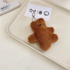 Close-up of a brown plush bear keychain with a silver chain on a cream tray
