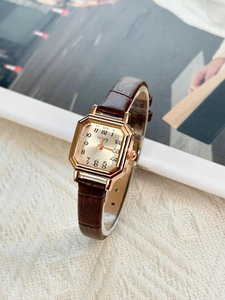 Detailed close-up of a square gold watch case with a brown leather strap and beige dial