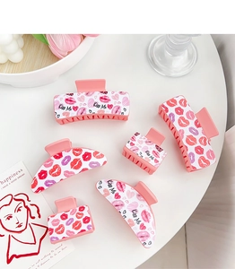 Detailed view of pink resin hair claws featuring red lip prints and Kiss Me text design
