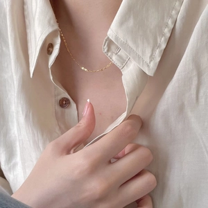 Detail of a minimalist gold pig-nose chain link necklace worn with a white linen shirt