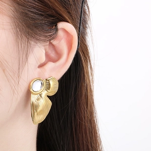 Detail view of a gold fan-shaped earring with irregular metal texture and a clear round gem