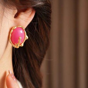 Détail d'une boucle d'oreille en résine rose avec cadre doré porté par un mannequin