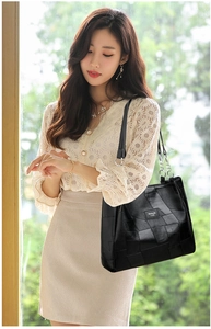 Detail of black tote bag with metal chain strap and brand label shown in lifestyle setting