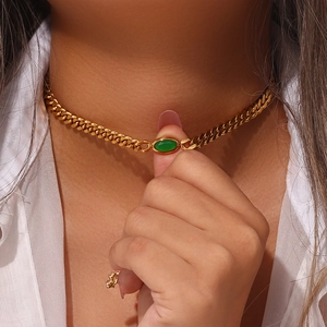 Close-up of golden Cuban link choker with an oval green gemstone on a model's neck