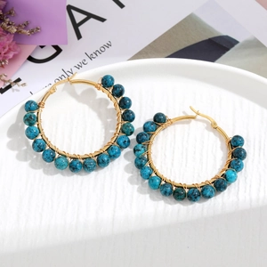 Detailed view of handmade gold wire wrapped earrings with blue stone beads on white tray