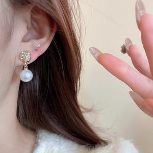 Close-up of elegant gold pearl earrings with sparkling rhinestones worn on a model ear