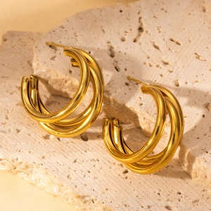 Minimalist triple-layer golden hoop earrings displayed on a textured stone background