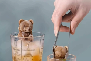 Detail view of silicone bear ice mold used for cocktail with metal tongs and glass cup