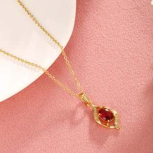 Close-up of golden necklace featuring a red oval gemstone pendant with diamond accents