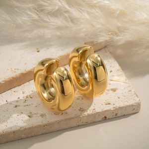 Detailed close-up of thick gold-plated C-shaped ear cuffs on a textured beige stone surface