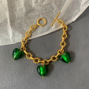 Detail of gold chain bracelet featuring green heart glass charms and a toggle clasp