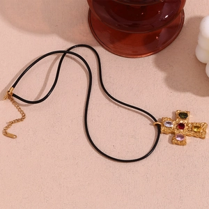 Detail of 18K gold cross pendant with colorful gems and black braided rope necklace