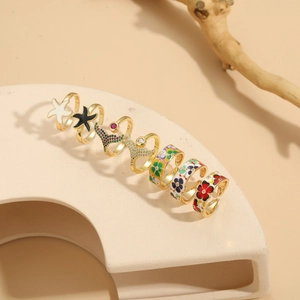 Détail macro de sept bagues dorées avec émail coloré et zircon sur socle beige