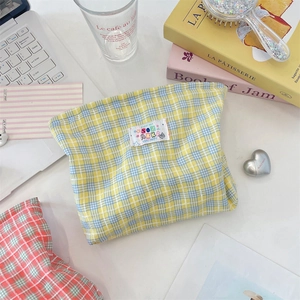 Dettaglio flatlay di una trousse da trucco in tela a quadri gialli con vari accessori
