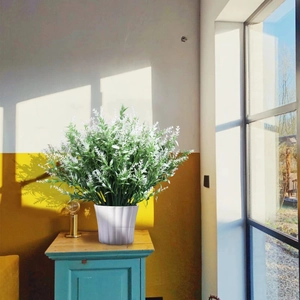 Artificial lavender in a white ribbed pot on a rustic blue cabinet with sunlight