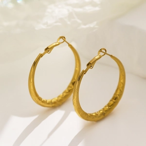Macro shot of gold hoop earrings with textured diamond pattern finish and high-gloss polish