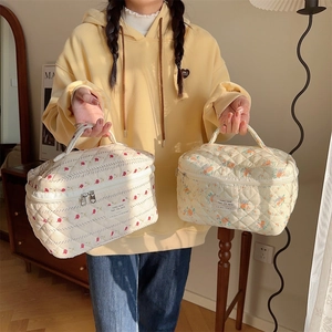 Détail de deux trousses de maquillage en coton matelassé à fleurs avec poignées de transport