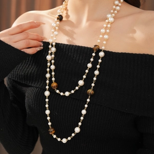 Detailed macro view of layered tiger eye beads and pearl necklace on a model