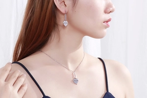 Close-up of silver heart-shaped MOM necklace and earrings set worn by a model