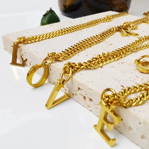 Detalle de colgantes de letras de acero inoxidable bañados en oro 14K en cadena Cuba