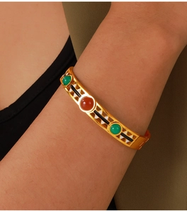 Close-up of vintage gold bangle with red and green stones and enamel detailing on wrist