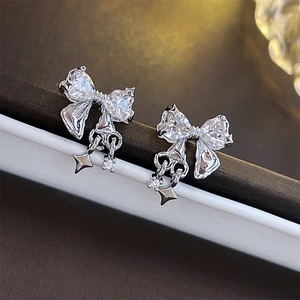 Close-up of silver bow stud earrings with sparkling zircons and a small star pendant