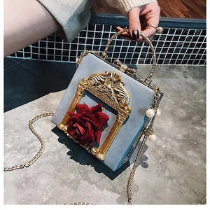 Detailed close-up of blue floral handbag featuring red roses, gold trim and pearl pendant