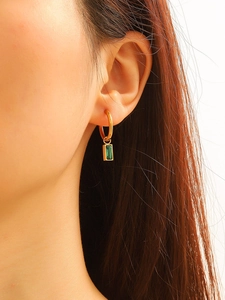 Close-up of gold-plated hoop earrings with emerald green rectangular gemstone on ear