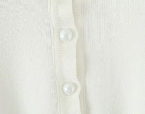 Dettaglio del cardigan in maglia bianca con eleganti bottoni rotondi perlati