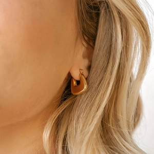 Close-up of a model wearing irregular gold geometric hoop earrings with a matte brushed finish