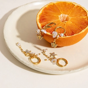 Détail de créoles plaquées or 18K avec breloques perles, papillons et étoiles