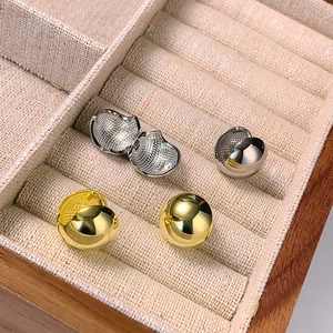 Macro shot of minimalist gold and silver ball hoop earrings in a beige velvet display box
