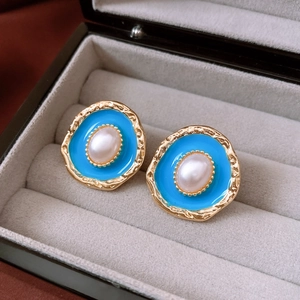 Close-up of vintage blue enamel and pearl earrings on a grey velvet jewelry box