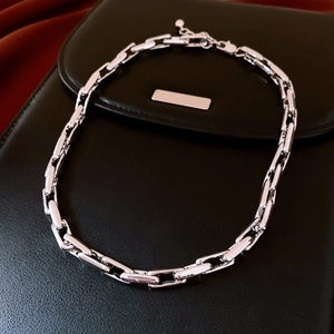 Macro detail of silver-tone chunky cable chain necklace on black textured leather surface