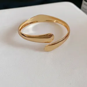 Polished gold metal open cuff bracelet featuring minimalist overlapping leaf design style