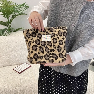 Detail of brown leopard print plush cosmetic bag held by a model in a home setting