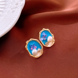 Detail of gold-tone butterfly earrings with blue resin fill and pearl accents on brown satin