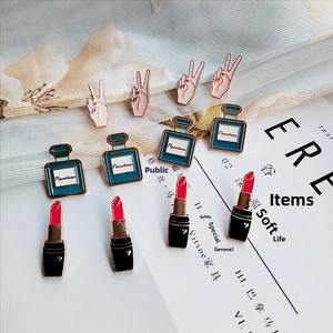 Close-up of enamel lipstick and perfume pins on soft fabric for fashion accessory detail