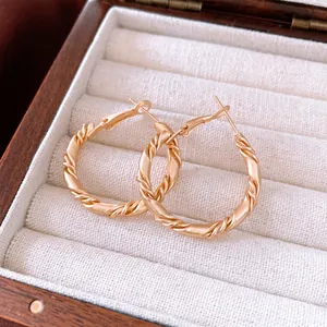 Luxurious gold-tone twisted hoop earrings with textured finish on a jewelry box liner